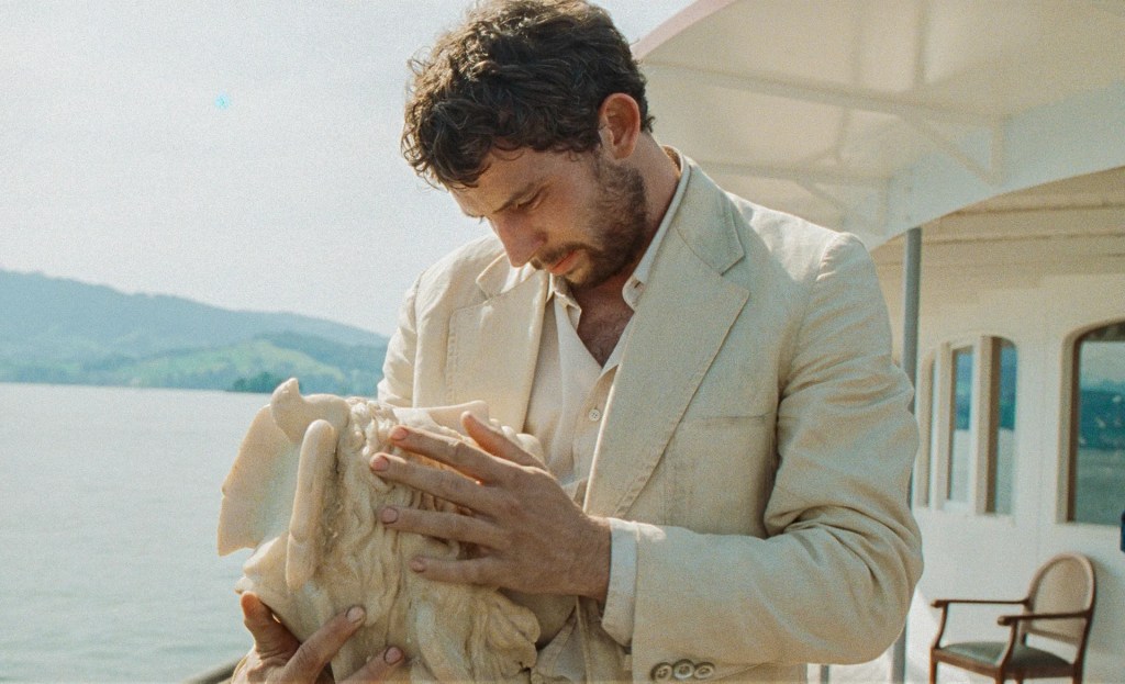 Arthur (Josh O'Conner) in a beige suit examining a classical sculpture
