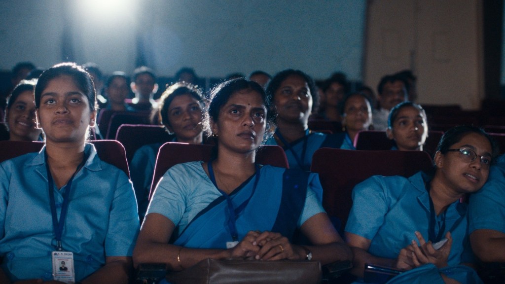 A group of people dressed in blue sit in a theatre, attentively watching something. 